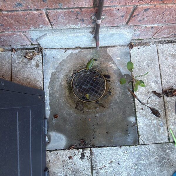 Image - External grated drain cleared beside the brick wall of the Stirling townhouse. External grated drain beside a brick wall and paved area at a townhouse in Stirling, Canberra